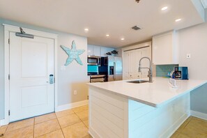 A modern kitchen with white cabinetry, a central island, and a starfish decoration on the wall. - Spacious, Beachy Condo At Waterscape Children's Playground, 2 Hot Tubs (Fort Walton Beach)