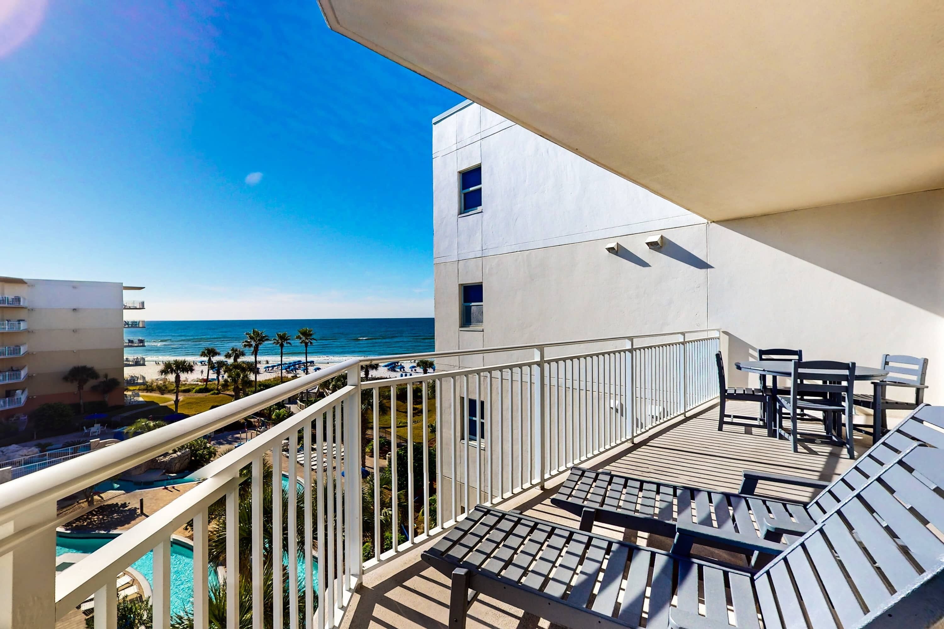 A balcony with a view of the ocean, a pool, and outdoor furniture.