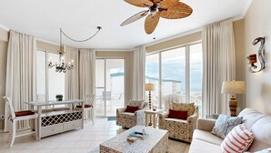 A spacious living room with a high ceiling fan, a dining area with a white table and chairs, and a sofa set. - Beach-view condo with outdoor pool, hot tub, sauna, tennis, BBQ, & beach access (Santa Rosa Beach)