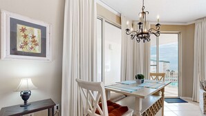 A dining area with a table, chairs, a chandelier, and a view of the outdoors. - Beach-view condo with outdoor pool, hot tub, sauna, tennis, BBQ, & beach access (Santa Rosa Beach)