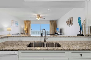 A kitchen with granite countertops, a double sink, a ceiling fan, and a view of the balcony. - Gorgeous and cozy beachfront condo with shared pool and beach access (Fort Walton Beach)
