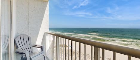 A balcony with a view of the ocean, a white chair, and a wooden table.