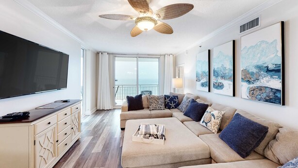 A modern living room with a large flat-screen TV, a beige sectional sofa, and a ceiling fan. - 4th-floor Gulf-front condo with pools - near entertainment (Perdido Key)