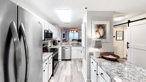 A modern kitchen with stainless steel appliances, white cabinets, and a granite countertop. - 4th-floor Gulf-front condo with pools - near entertainment (Perdido Key)