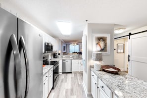 A modern kitchen with stainless steel appliances, white cabinets, and a granite countertop. - 4th-floor Gulf-front condo with pools - near entertainment (Perdido Key)