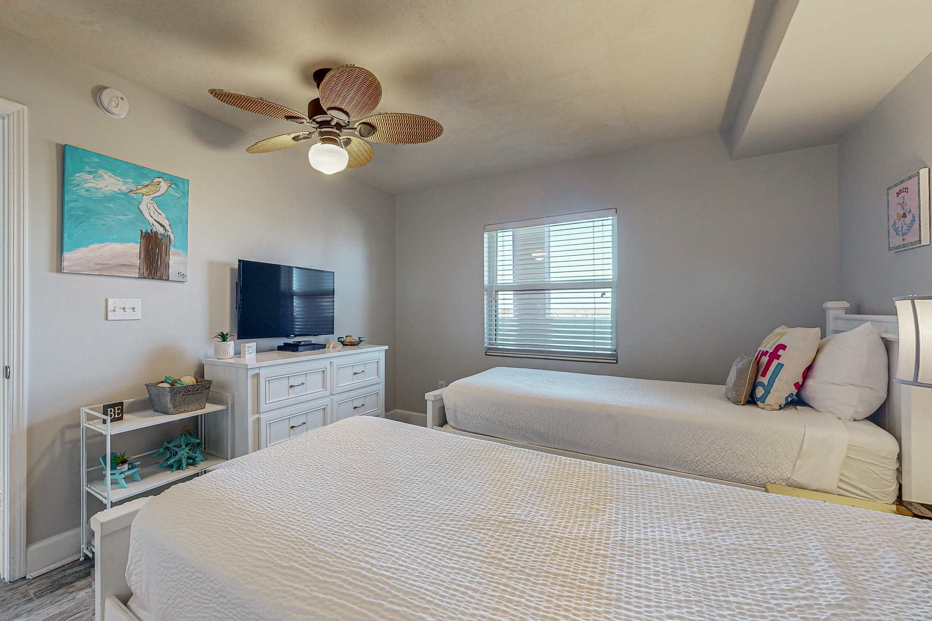 A bedroom with two beds, a ceiling fan, a television, and a window with blinds.