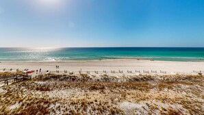 A beach with a wooden walkway leading to the water, a sandy area with sparse vegetation, and a clear blue sky. - Oceanfront condo with pool, hot tub, central AC, washer&dryer, & fitness room (Fort Walton Beach)