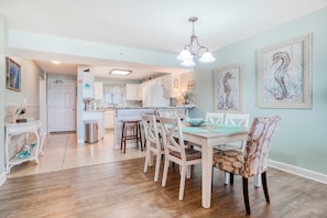 A dining area with a white table and chairs, a chandelier, and artwork on the walls. - Gorgeous Oceanfront condo with washer/dryer, Gulf-front balcony & pool/hot tub (Perdido Key)
