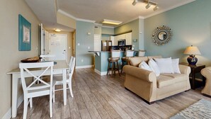 Ein Wohnzimmer mit einem beigen Sofa, einem Esstisch mit Stühlen und einer Küche im Hintergrund.