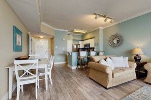A living room with a beige sofa, a dining table with chairs, and a kitchen in the background. - High-end retreat with balcony, sweeping Gulf views, pools & hot tubs (Panama City Beach)