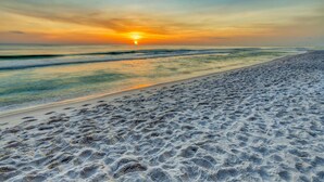 Ein Strand mit Fußabdrücken im Sand und einem Sonnenuntergang im Hintergrund.