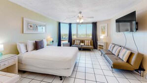 Ein Hotelzimmer mit einem großen Bett, einer Couch, einem Fernseher und einem Balkon mit Blick.