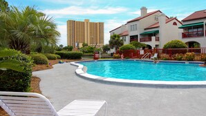 A swimming pool with a curved edge, surrounded by a red fence, and a white lounge chair in the foreground. - Cozy condo in paradise with pool, sauna & private dock - snowbird-friendly (Panama City Beach)