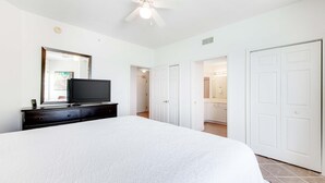 A bedroom with a large bed, a TV on a dresser, a ceiling fan, and white doors leading to other rooms. - 16th-floor waterfront condo with fast WiFi, Gulf view, pools, hot tubs, & gym (Panama City Beach)