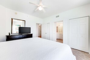 A bedroom with a large bed, a TV on a dresser, a ceiling fan, and white doors leading to other rooms. - 16th-floor waterfront condo with fast WiFi, Gulf view, pools, hot tubs, & gym (Panama City Beach)
