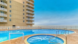 A swimming pool area with a hot tub, surrounded by a brick deck, and adjacent to a high-rise building. - 16th-floor waterfront condo with fast WiFi, Gulf view, pools, hot tubs, & gym (Panama City Beach)