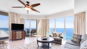 A spacious living room with a large TV, a ceiling fan, and a view of the ocean. - 16th-floor waterfront condo with fast WiFi, Gulf view, pools, hot tubs, & gym (Panama City Beach)