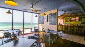 Ein Restaurant mit Tischen, Stühlen und einer Bar, mit Blick auf den Ozean.
