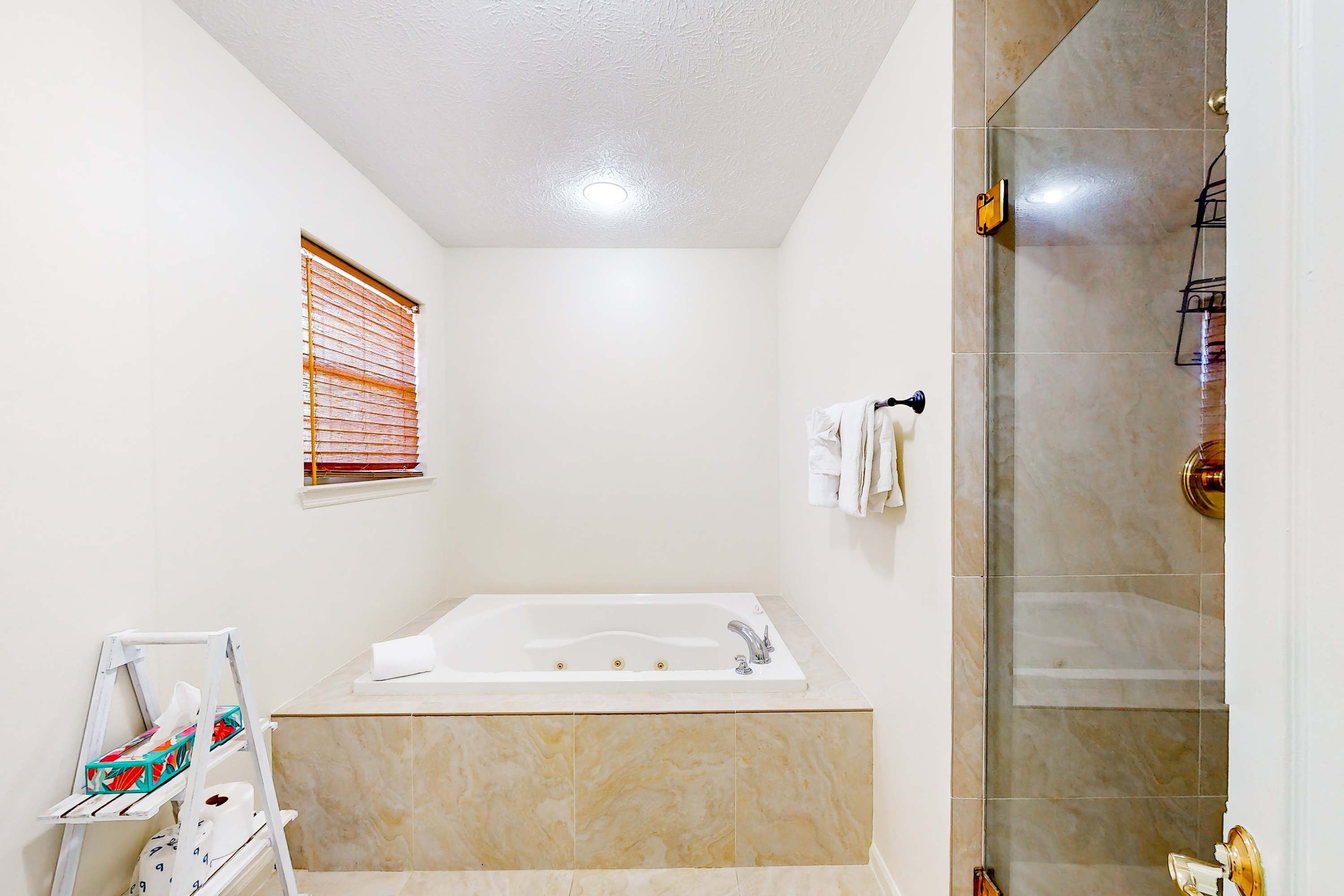 Un baño moderno con una bañera grande, un box de ducha de vidrio y una ventana pequeña con persianas.