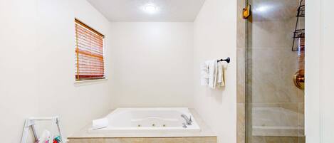 Un baño moderno con una bañera grande, un box de ducha de vidrio y una ventana pequeña con persianas.