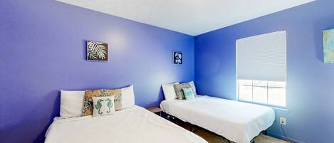 A room with two beds, a window with blinds, and two wall-mounted artworks.
