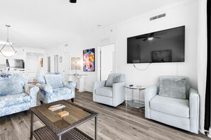 A modern living room with a flat-screen TV, two sofas, a coffee table, and a ceiling fan. - Beachfront penthouse with 2 free beach chairs, WiFi, amazing views, pool & hot tub (Panama City Beach)