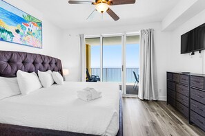 A bedroom with a large bed, a ceiling fan, a TV, a balcony with a view, and a painting on the wall. - Beachfront penthouse with 2 free beach chairs, WiFi, amazing views, pool & hot tub (Panama City Beach)