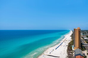 A beachside hotel with a long sandy beach, a pool area, and a tall building adjacent to the beach. - Beachfront penthouse with 2 free beach chairs, WiFi, amazing views, pool & hot tub (Panama City Beach)