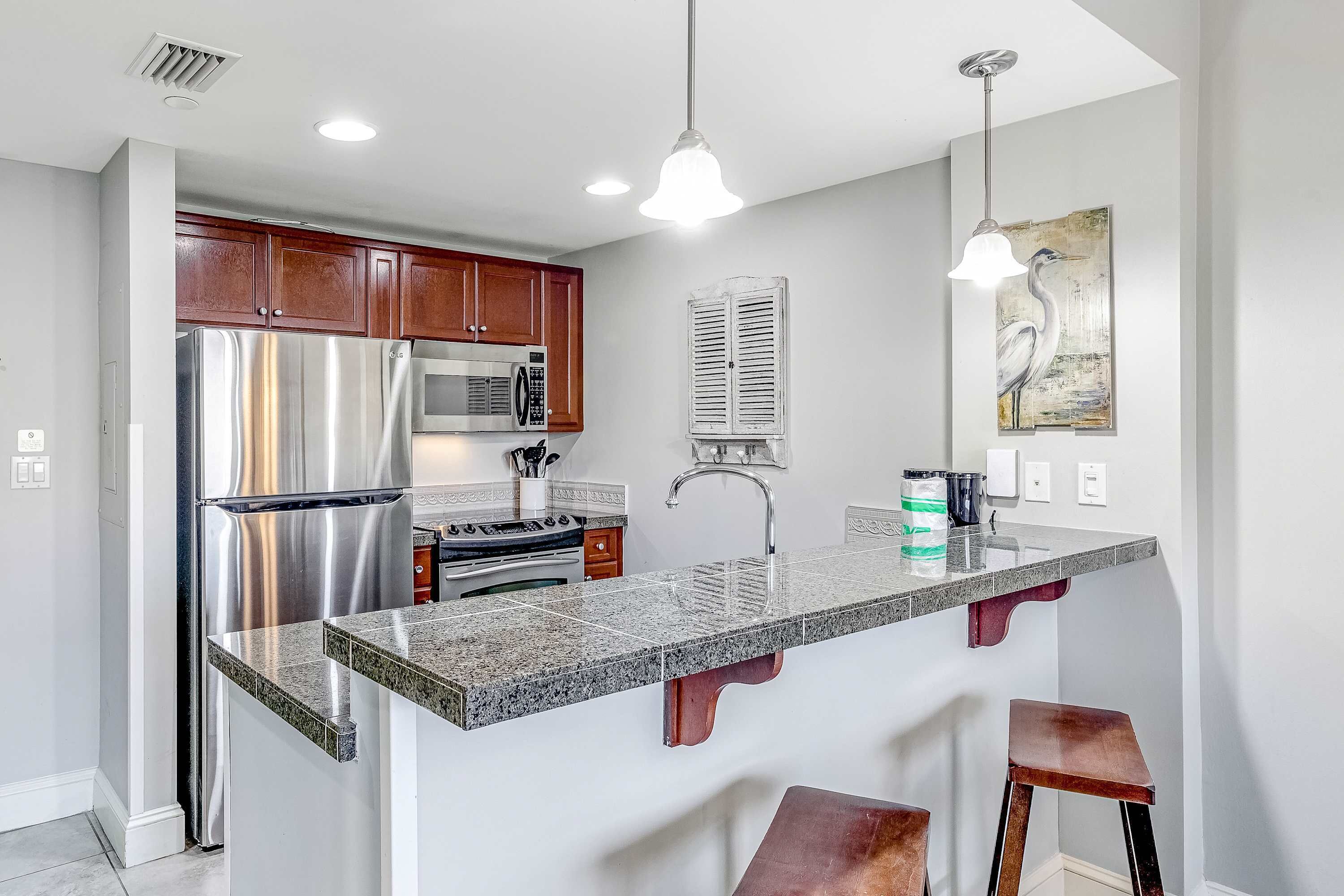 A modern kitchen with stainless steel appliances, a granite countertop, wooden cabinets, and pendant lighting.