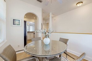 A round glass table with wicker chairs, a white vase with flowers, and a kitchen in the background. - 2BR Blue Mountain Beach Condo | Shared Pool | Gym | 2 Bikes (Santa Rosa Beach)