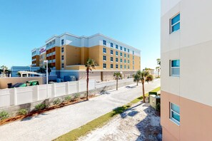 A multi-story hotel with balconies, a parking area, and palm trees. - Inviting, Spacious Condo On Okaloosa Island Playground, 2 Hot Tubs (Fort Walton Beach)