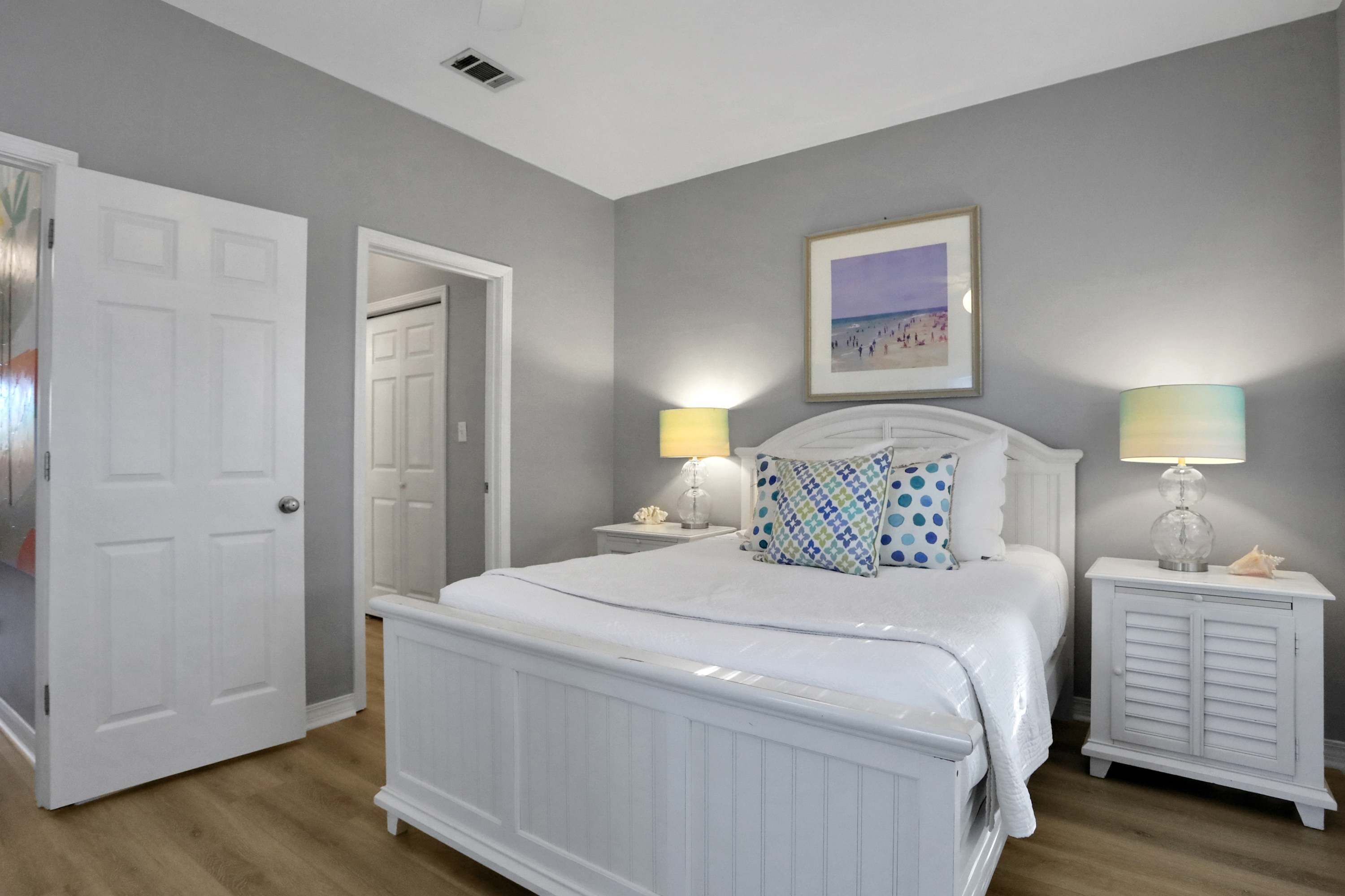 A bedroom with a large bed, two bedside tables with lamps, a door, and a framed picture on the wall.