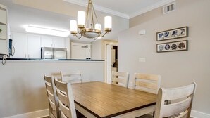 Un comedor con una mesa y sillas de madera, una araña y una cocina al fondo.