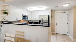 Una cocina moderna con armarios blancos, encimera negra, electrodomésticos de acero inoxidable y una luz empotrada en el techo.