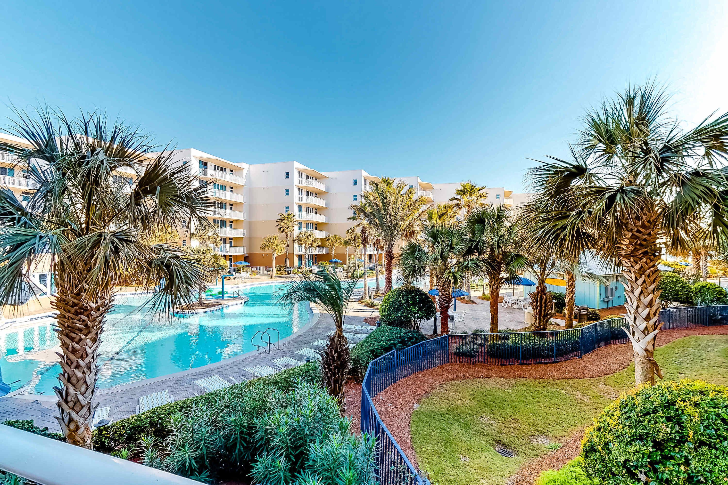 A resort with a swimming pool, palm trees, and a building with balconies.