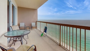 A balcony with a glass table and chairs, overlooking a beach. - Gulf-front condo with high-speed WiFi, pools, hot tubs & beach access (Panama City Beach)