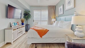 A bedroom with a bed, a TV, a ceiling fan, a window with curtains, and a plant. - Gulf-front condo with high-speed WiFi, pools, hot tubs & beach access (Panama City Beach)