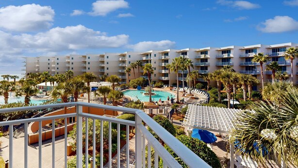 Ein Resort mit Swimmingpool, Palmen und einem mehrstöckigen Gebäude mit Balkonen.
