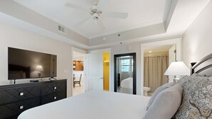 Ein Hotelzimmer mit einem Bett, einem Fernseher, einem Deckenventilator und einem durchgegangenen Türspalte erkennbaren Badezimmer.