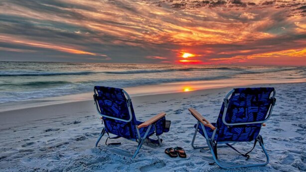 Twee strandstoelen gericht op de oceaan met een zonsondergang op de achtergrond.