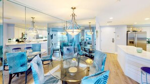 Een moderne keuken met een centraal eiland, een glazen eettafel en blauwe bekleden stoelen.