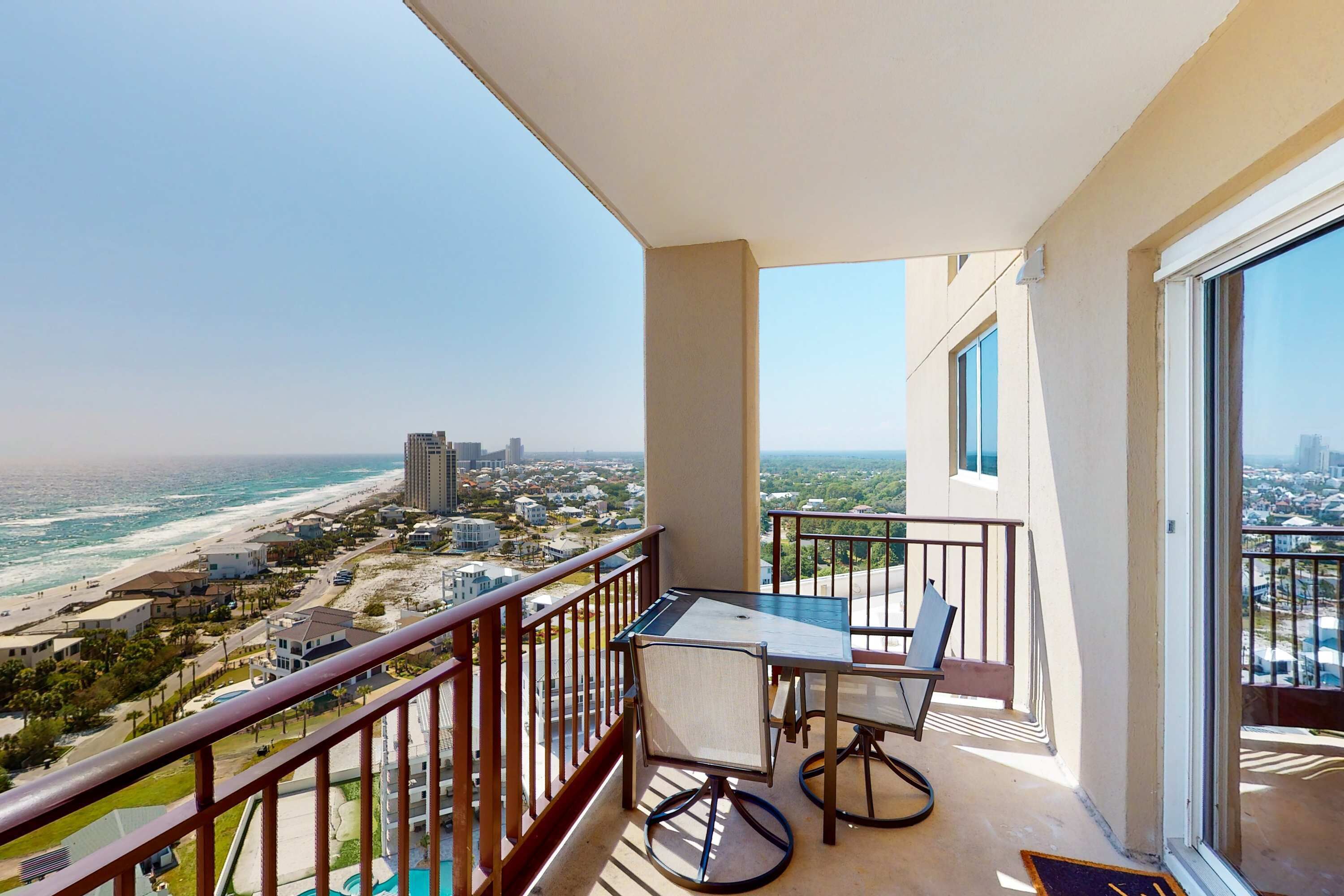 A balcony with a table and chairs, overlooking a beach and cityscape.