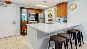 A modern kitchen with a large island, bar stools, stainless steel appliances, and wooden cabinets. - 3rd Floor Spacious Condo At Waterscape Children's Playground, 2 Hot Tubs (Fort Walton Beach)