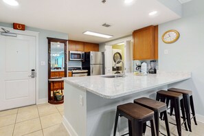 A modern kitchen with a large island, bar stools, stainless steel appliances, and wooden cabinets. - 3rd Floor Spacious Condo At Waterscape Children's Playground, 2 Hot Tubs (Fort Walton Beach)