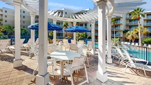 A poolside area with white lounge chairs, blue umbrellas, and a pool. - 3rd Floor Spacious Condo At Waterscape Children's Playground, 2 Hot Tubs (Fort Walton Beach)