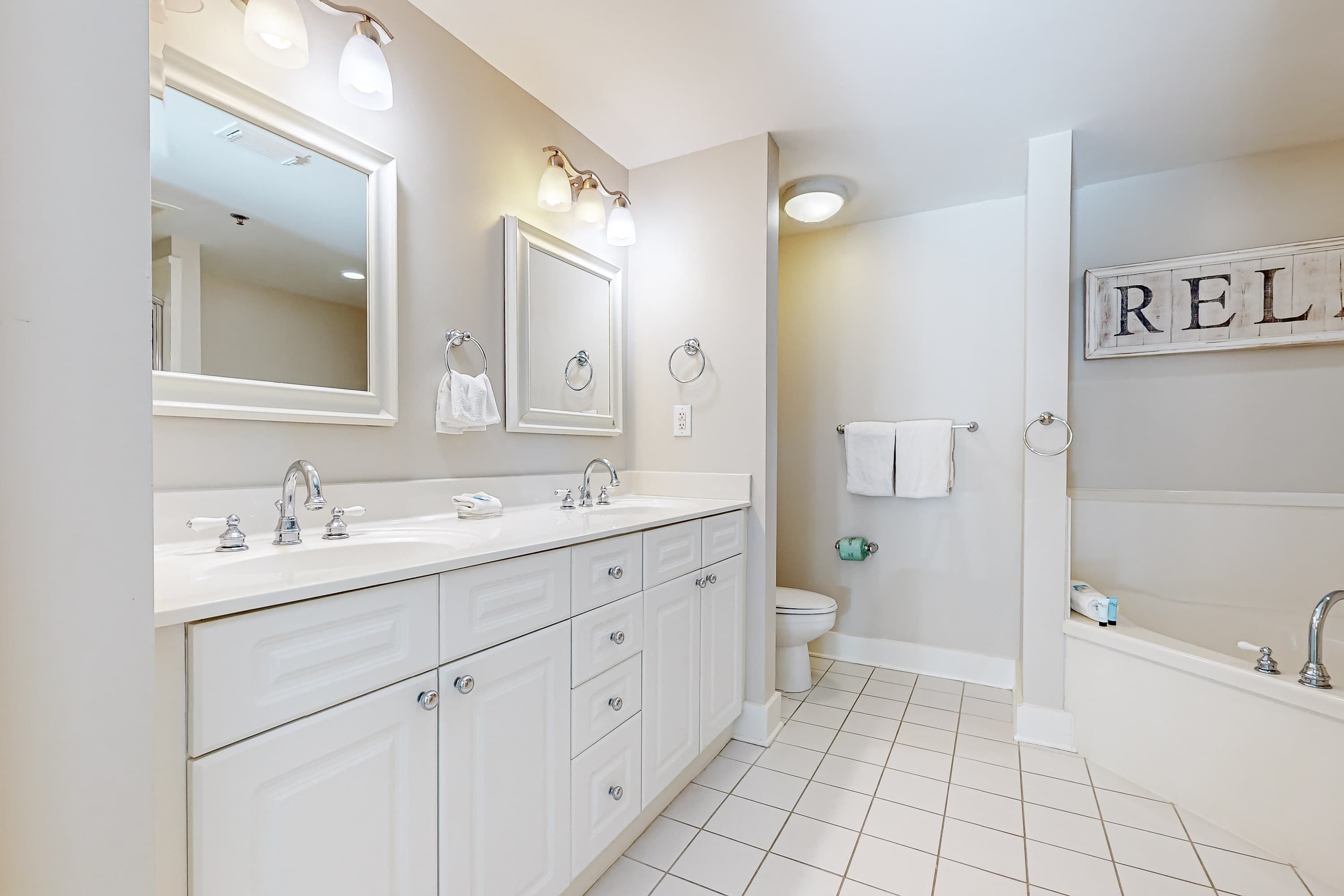 A modern bathroom with a large mirror, dual sinks, a toilet, and a bathtub.