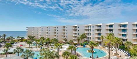 A hotel with multiple floors, a swimming pool, and palm trees.