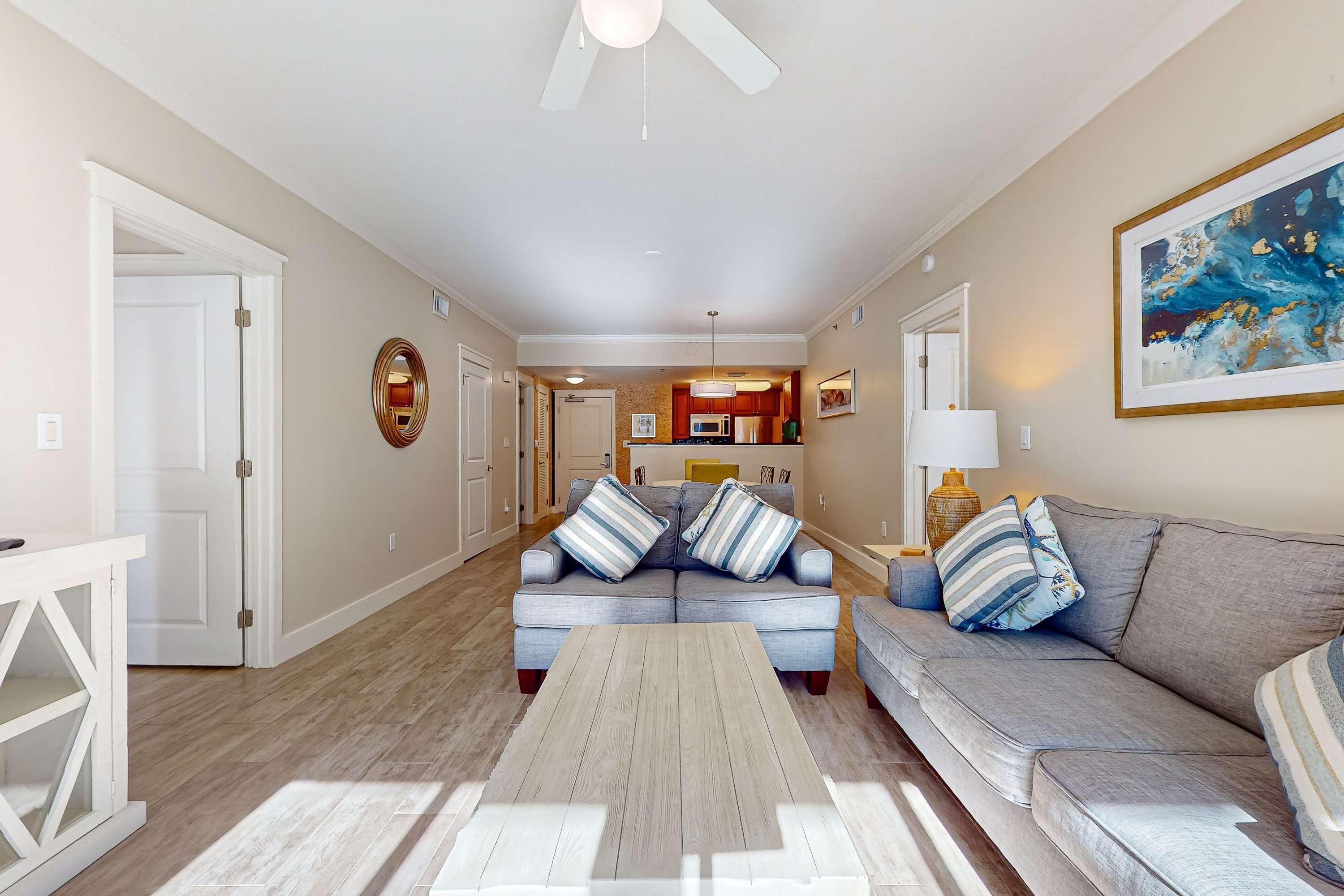 A spacious living room with a grey sectional sofa, a wooden coffee table, and a kitchen in the background.