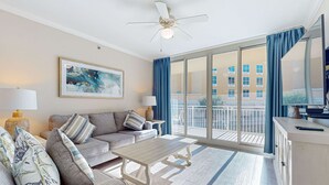 A spacious living room with a sofa, coffee table, and a balcony with a view of buildings. - 2nd Floor Waterscape Condo w Beach Access, Beach Service, Shared Amenities (Fort Walton Beach)