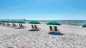 A beach with rows of lounge chairs and green umbrellas, a pier in the background, and clear skies. - 2nd Floor Waterscape Condo w Beach Access, Beach Service, Shared Amenities (Fort Walton Beach)